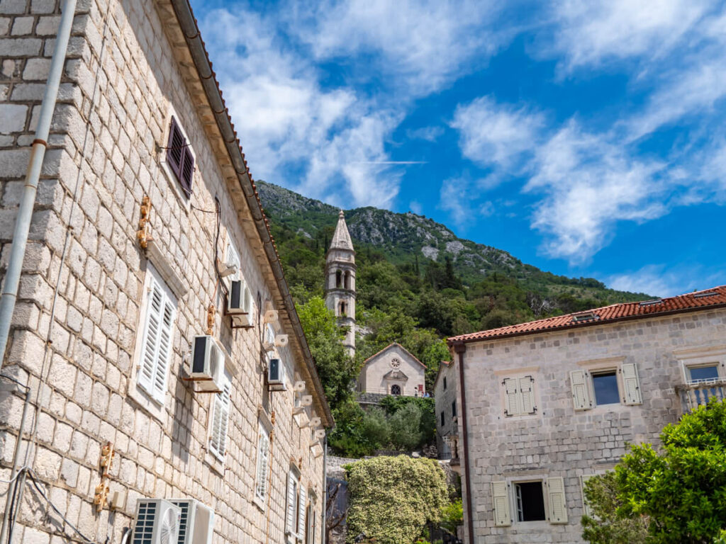 Stone buildings backed by a church on a green hill in Perast, Montenegro.