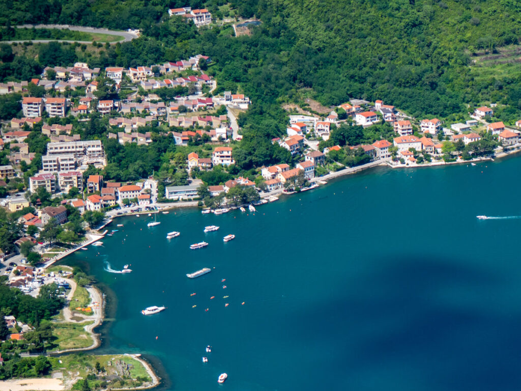 Kotor Bay in Montenegro. The red roofs of waterfront hotels and restaurants reflect the sunlight, and a handful of boats are sitting in the water.