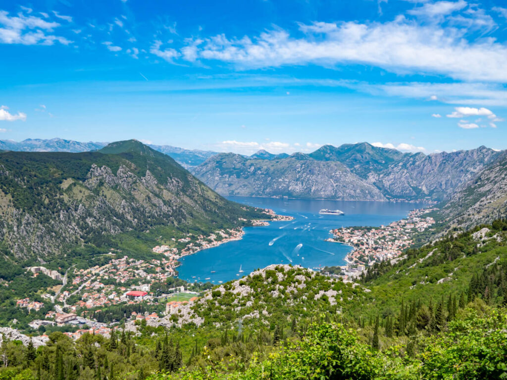 A view of the blue Bay of Kotor surrounded by small towns and hilly greenery.