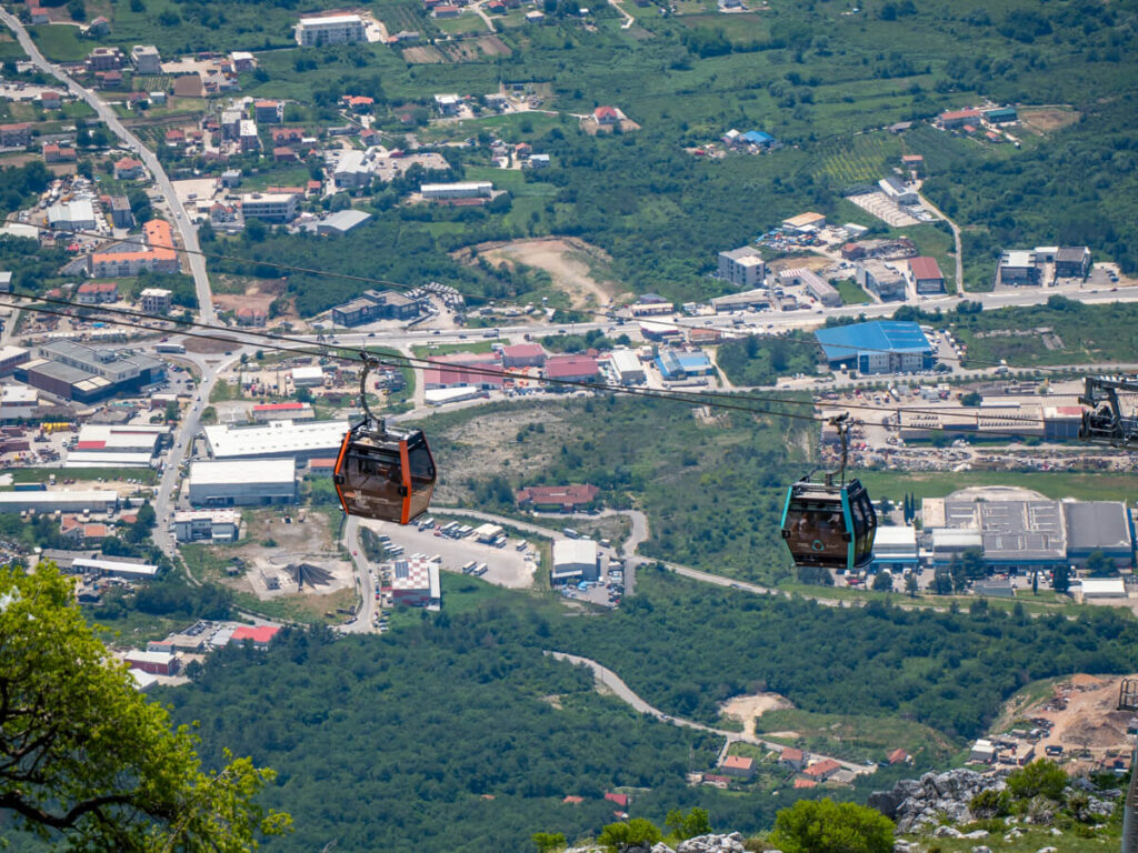 Blue and red gondolas on a cable car suspended against a backdrop of Kotor.