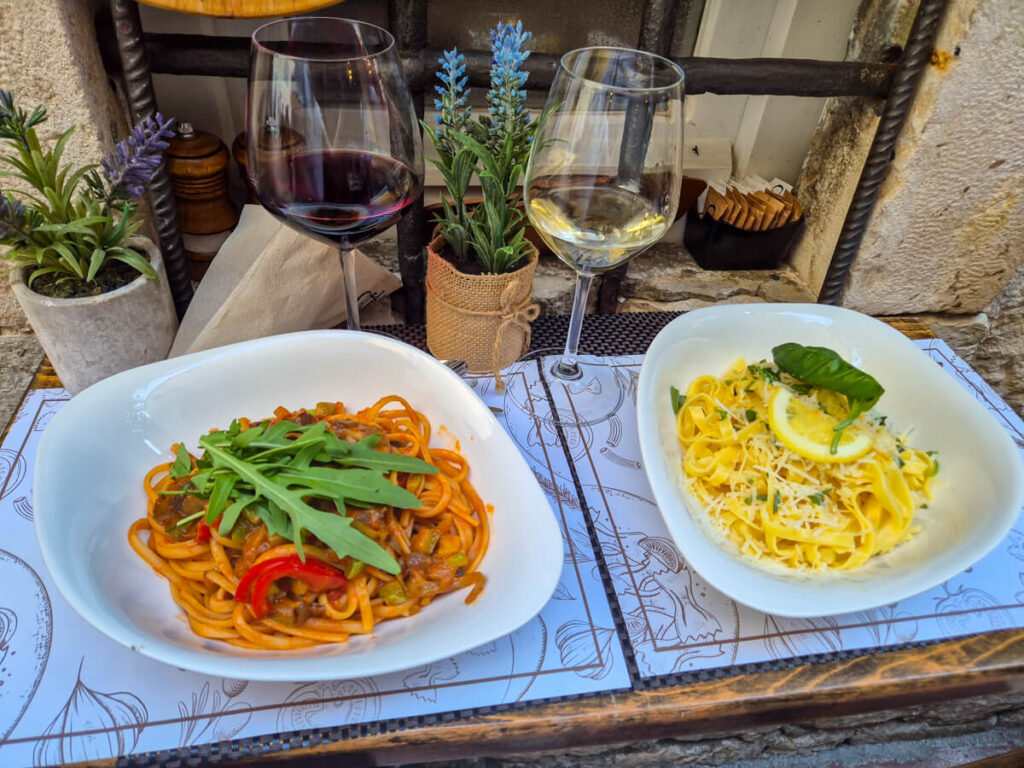 Two glasses of wine and two plates of pasta on a table at La Catedral Pasta Bar, one of the best restaurants in Kotor.