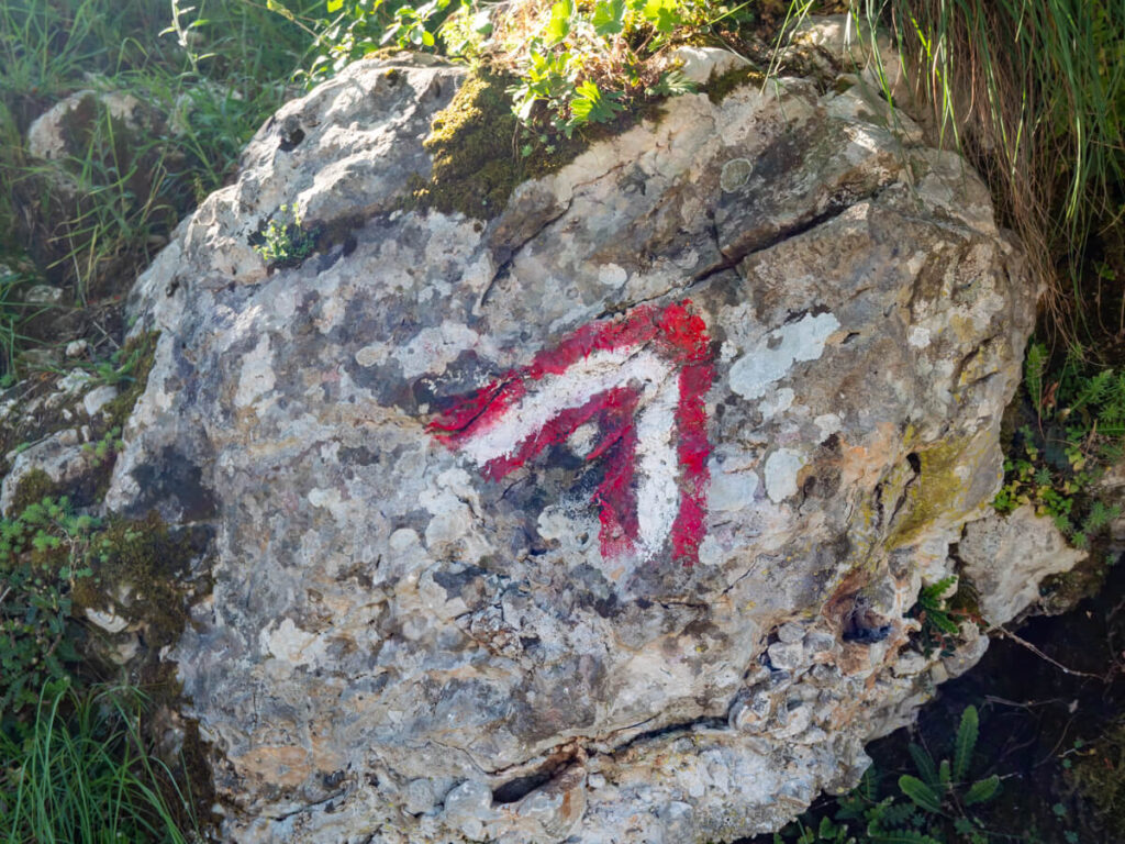 An arrow-shaped red and white trail marker painted on a stone on the Ladder of Kotor trail.