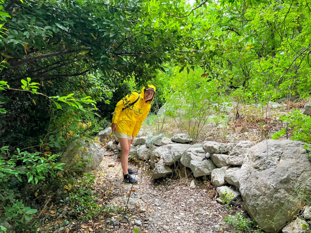 Lucy in a yellow coat walking through a forest in Lipci to the rock art.