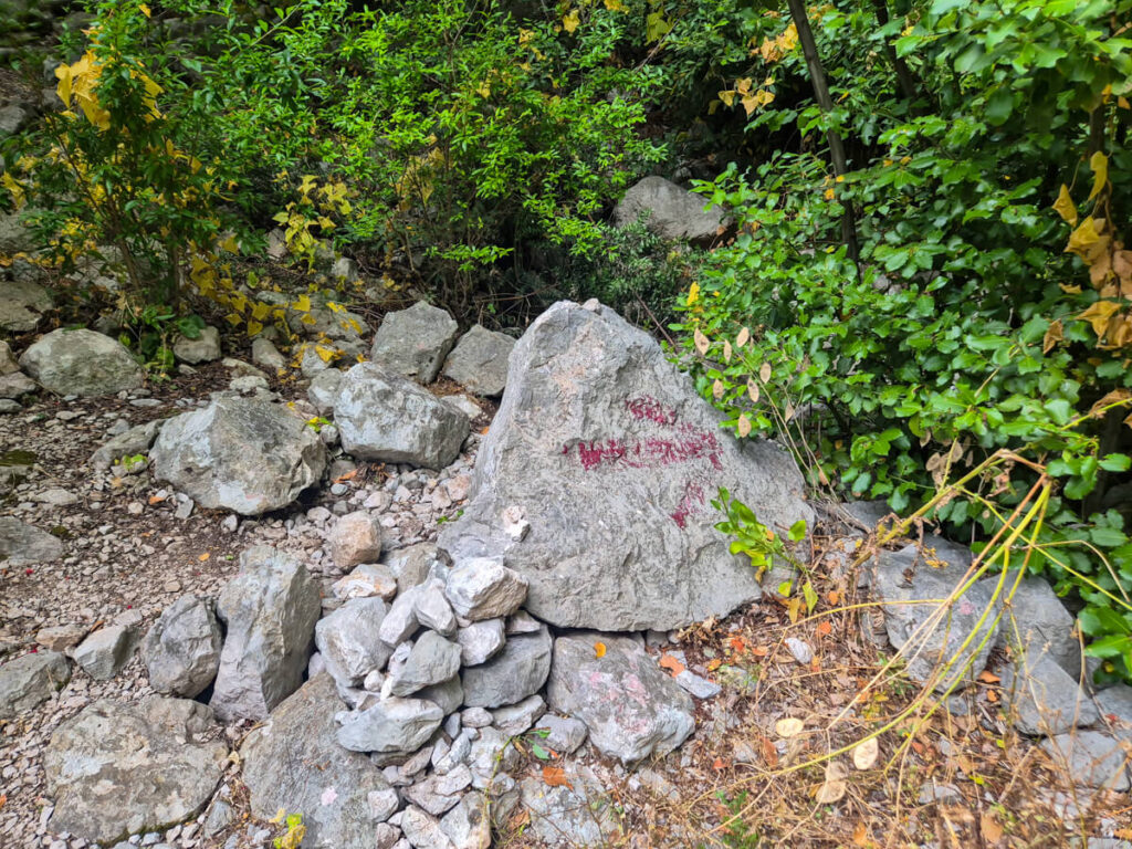 A red arrow painted on a boulder in a forest, pointing to the right along the trail to the Lipci rock art.