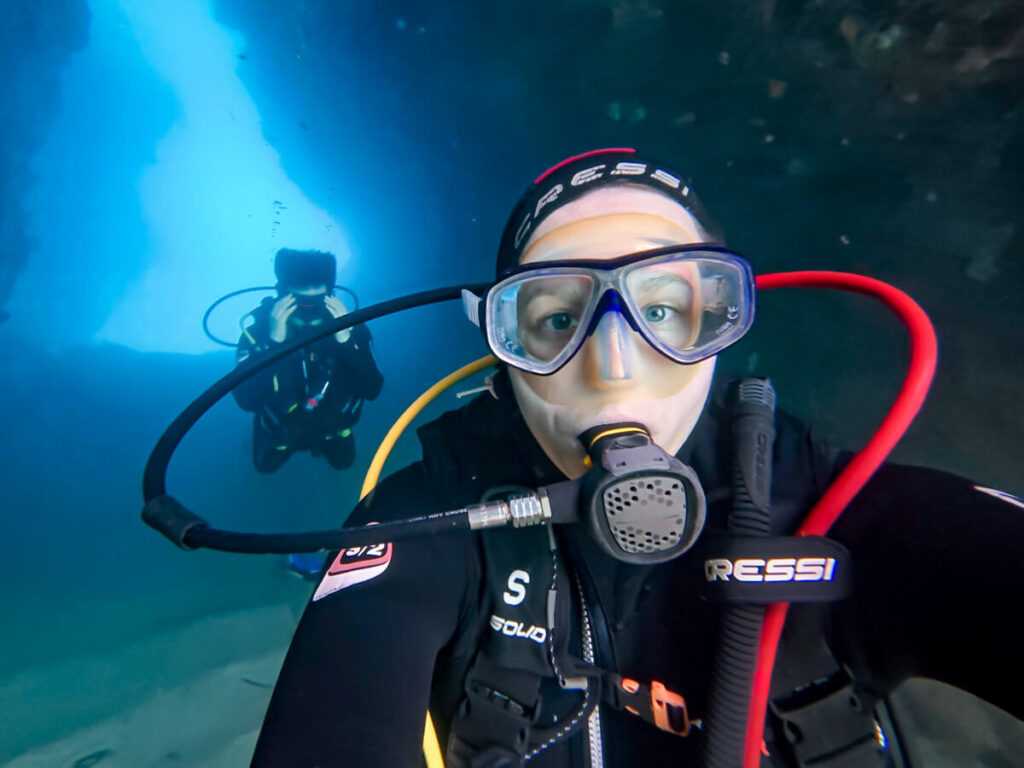 Lucy SCUBA diving through a tunnel near Budva, with Dan swimming behind her.