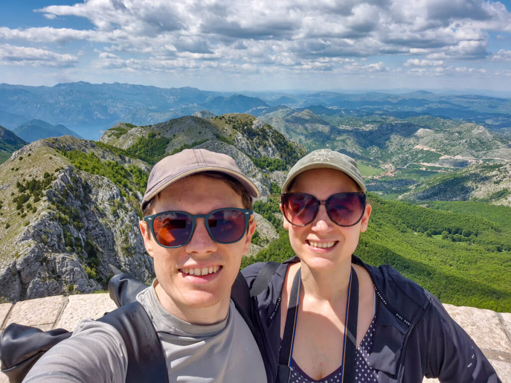 Lucy and Dan smiling at the camera in Lovćen National Park, backed by rolling green mountains.