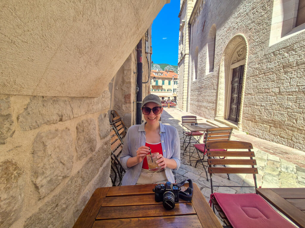 Lucy sitting at an outdoor table near St Tryphon's Cathedral in Mon Bistro Cafe in Kotor.