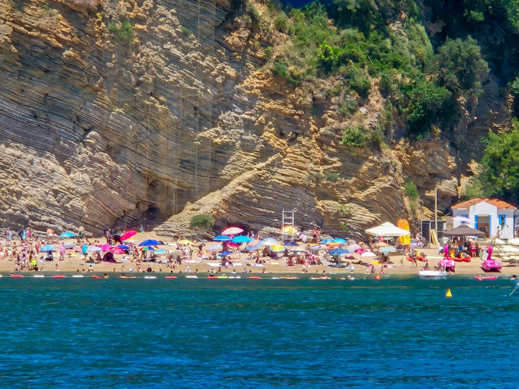 Lots of sunbathers and multi-coloured umbrellas on Mogren Beach in Budva,