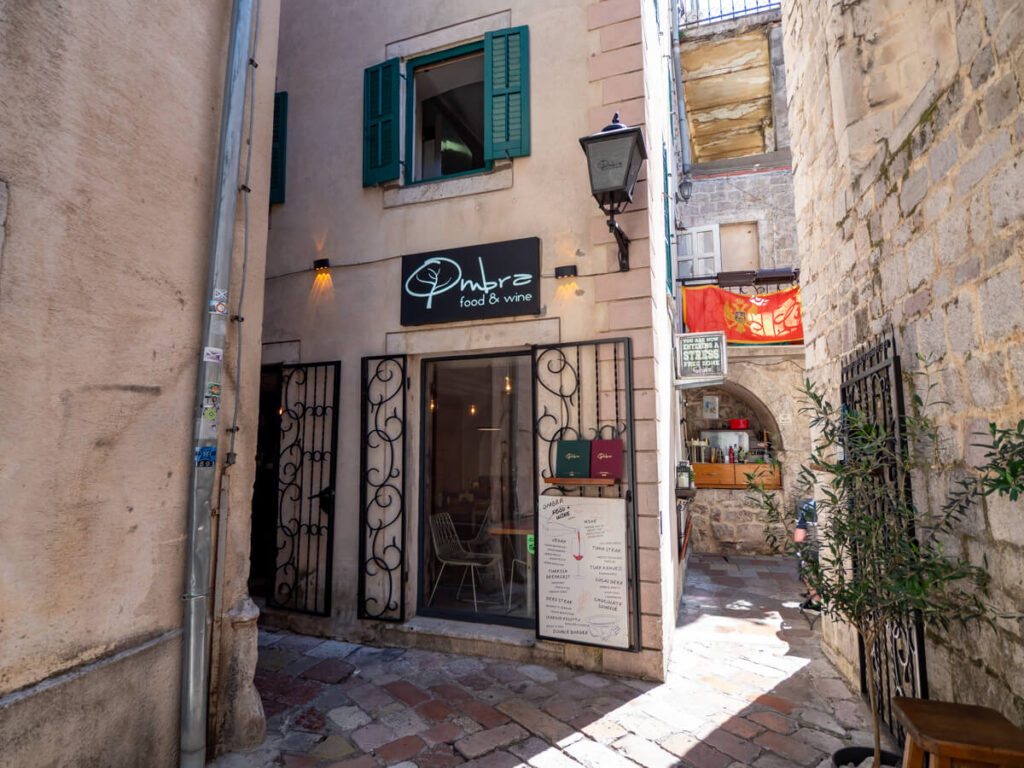 A sign above a doorway reading "Ombra", restaurant down a narrow stone street in Kotor's Old Town.