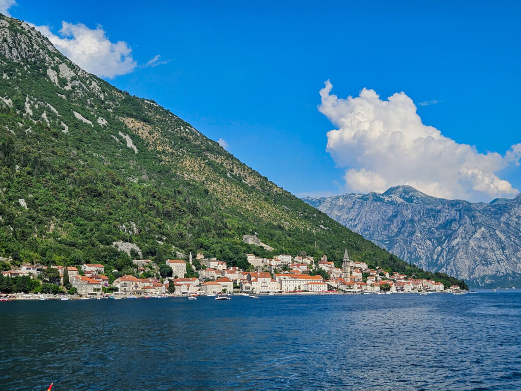 Houses lining the waterfront of a lush mountain in the Bay of Kotor, viewed from yhe water.