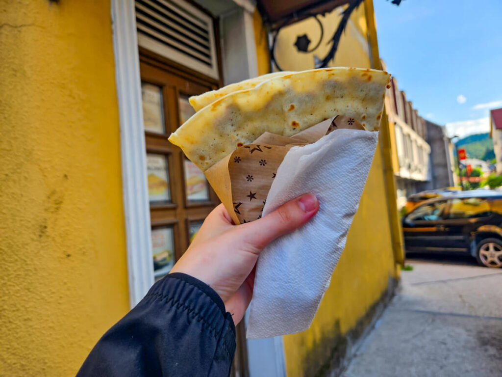 A hand holding a palacinke in front of a café in Cetinje.