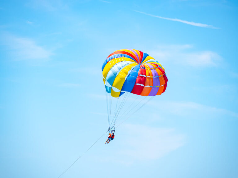 A couple parasailing under a multi-coloured balloon against the blue sky.