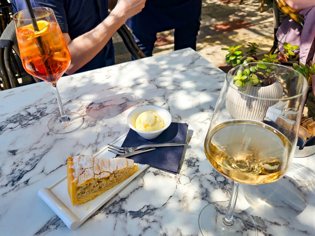 A plate of Perast Cake, a glass of wine, and an Aperol Spritz in a café in Perast, Montenegro.