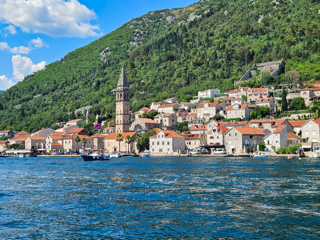 Perast waterfront lined with stone houses and churches, viewed from a boat on the water.