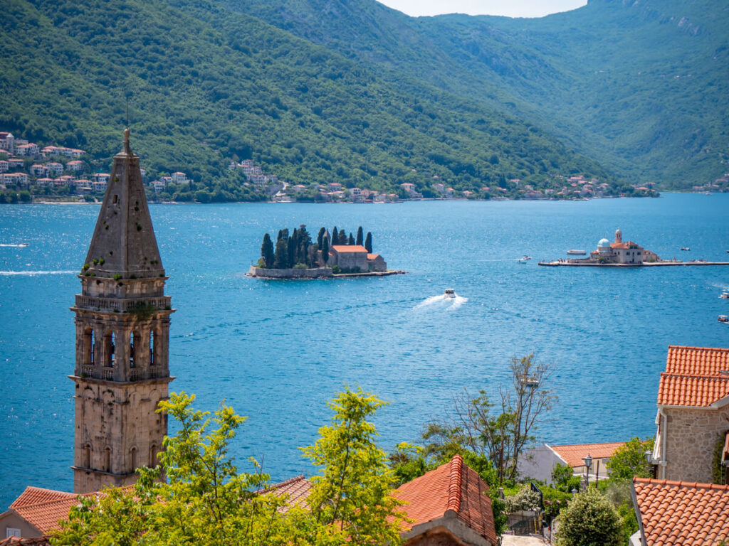 A church tower backed by sparkling blue sea and two small islands off the coast of Perast, Montenegro.