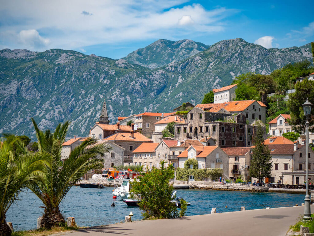 Houses lining Perast's promenade lined with palm trees and backed by mountains.