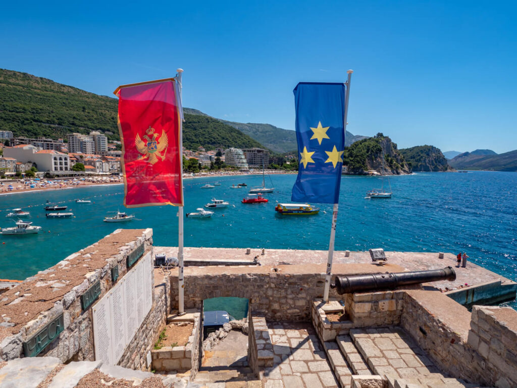 A Montenegrin flag and the Flag of Budva on Petrovac Fortress overlooking the town and beach,