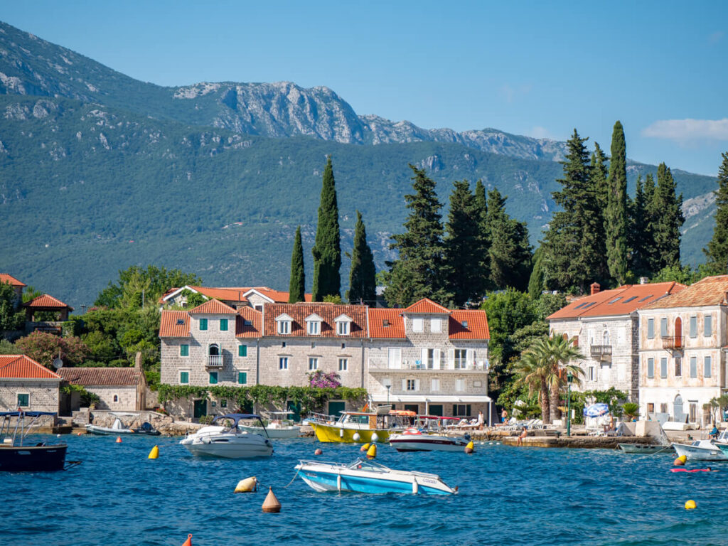 Boats moored in front of the waterfront of Rose, Montenegro, lined with stone houses.
