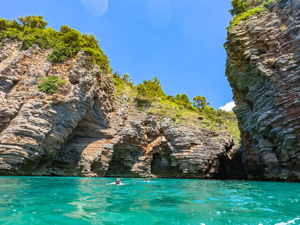 Two snorkellers in the clear waters of a dive site near Mogren Beach, backed by cliffs, in Budva, Montenegro