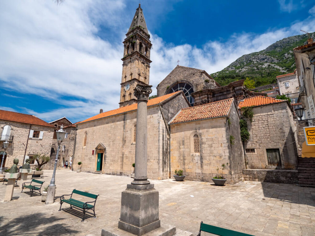 A Roman column and busts of famous figures in the main square in Perast, overlooked by the bell tower of Saint Nicholas Church.