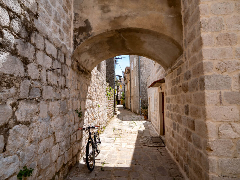 A bicycle under a stone arch leading down a street in Perast, Montenegro.