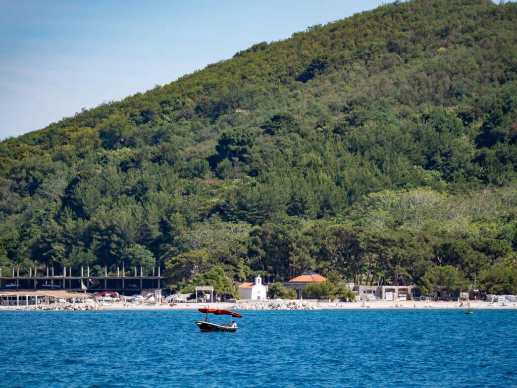 A small boat bobbing in the sea in front of a sandy beach and small white church.