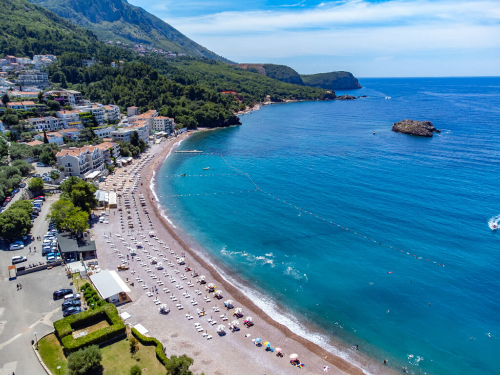 An aerial photo of sun loungers on Sveti Stefan Beach, backed by the town and overlooking the blue Adriatic Sea.