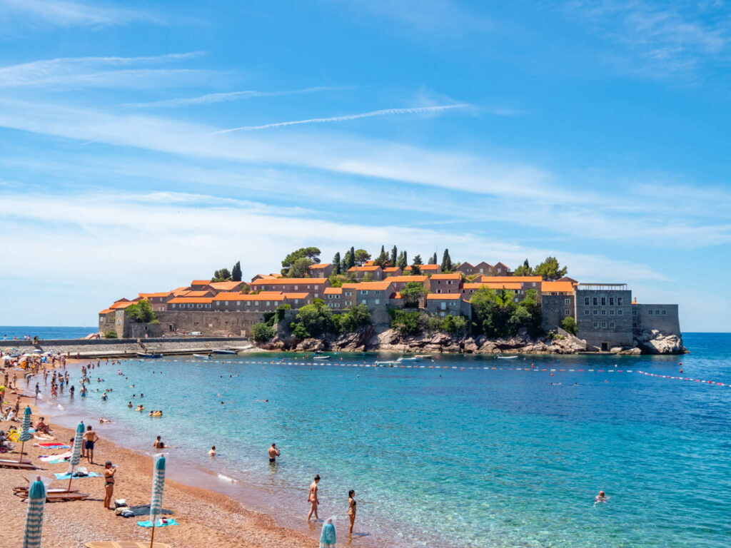 People on a beach in front of Sveti Stefan Island.