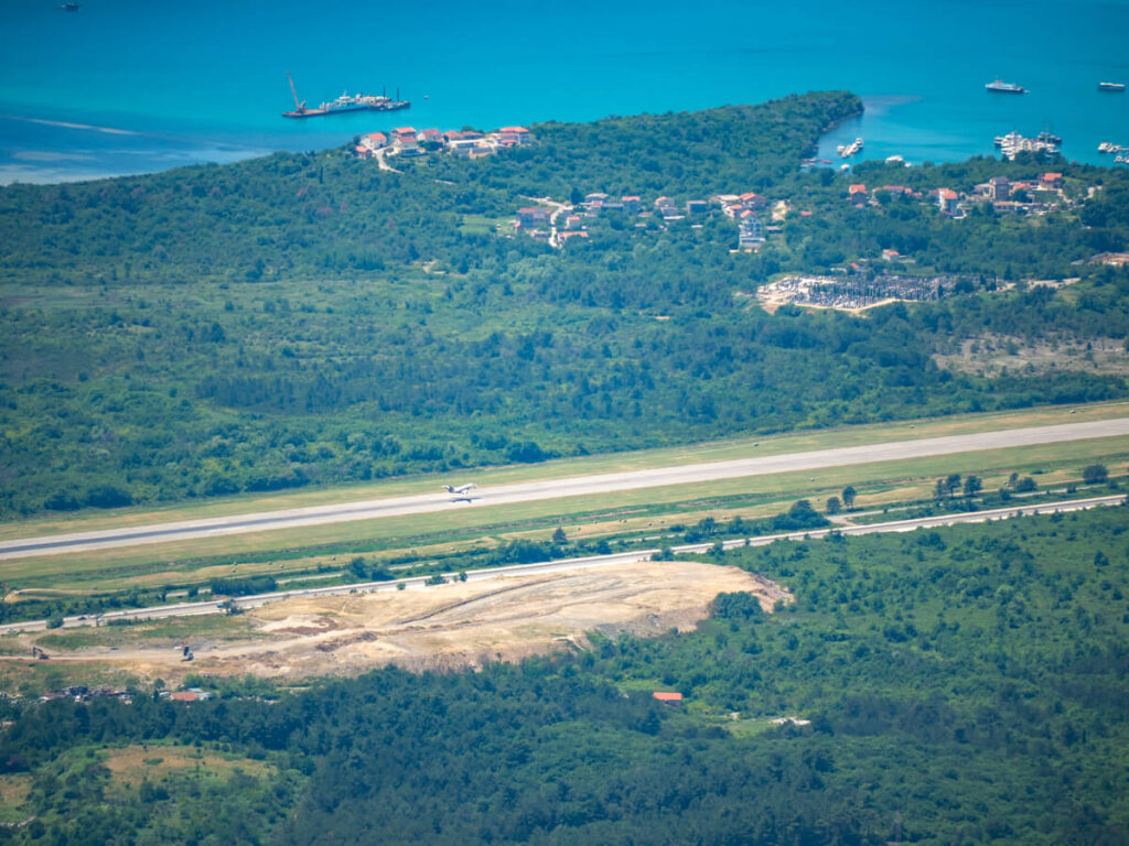 A plane taking off from the runway at Tivat Airport, surrounded by the Bay of Kotor.