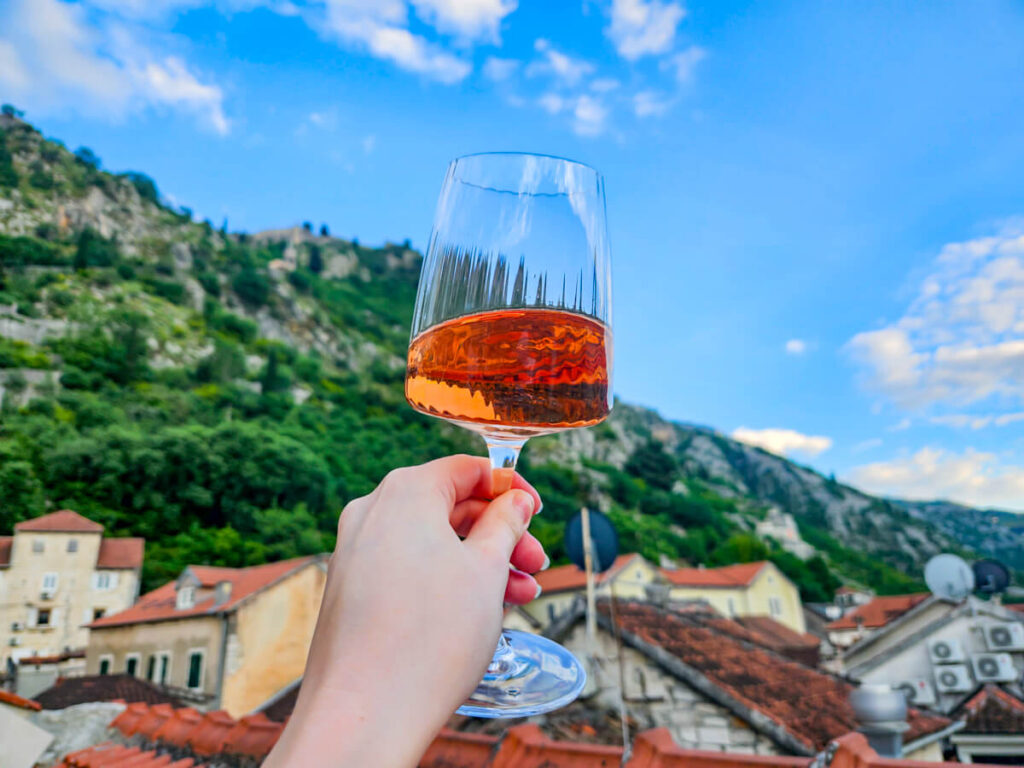 A hand holding a glass of rose wine in front of the mountains, seen from the rooftop at in Kotor's Hotel Hippocampus.